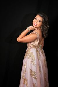 Portrait of young woman standing against black background