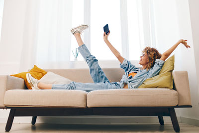 Rear view of man with arms raised sitting on sofa at home