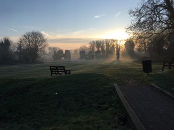 Park bench on field against sky during sunset