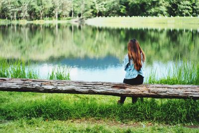 Woman sitting on grass by lake against trees