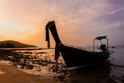 Boat moored on beach against sky during sunset