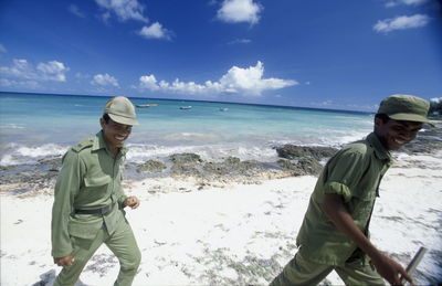Portrait of smiling security guards walking at beach against sky