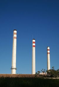 Low angle view of smoke stacks against clear blue sky
