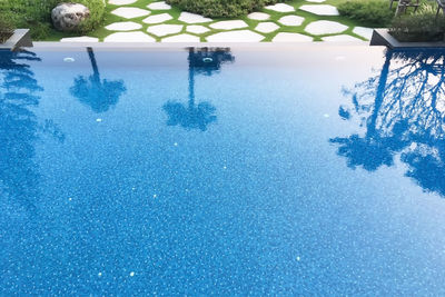 Swimming pool by trees against blue sky