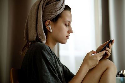 Teenage girl in turban made of towels in living room looks in smartphone