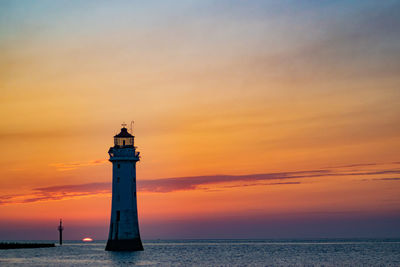 Lighthouse by sea against sky during sunset