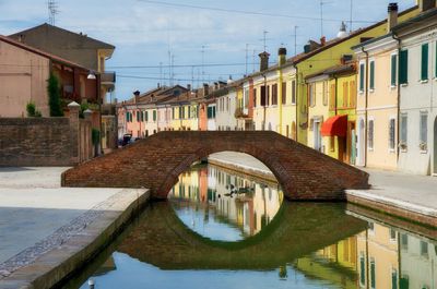 Arch bridge over canal amidst buildings against sky