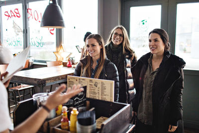 Smiling female friends looking at owner in restaurant