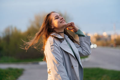 Beautiful smiling girl with long hair in a grey trench coat outdoors on the street spring