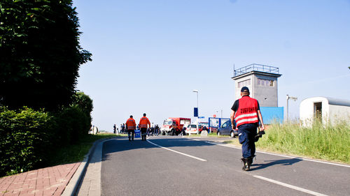 Rear view of male firefighters walking on road against sky