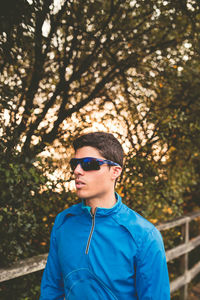 Portrait of young man wearing sunglasses standing against plants
