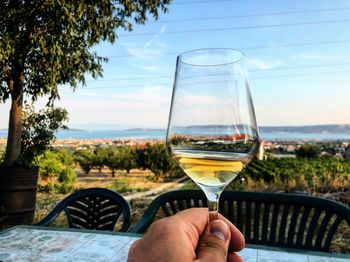 Person hand holding glass of drink against sky