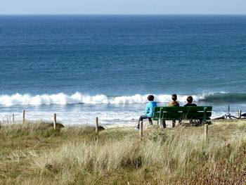 Rear view of friends sitting on bench at beach