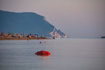 Group of people on sea shore against sky. the conero seen from porto recanati at dawn