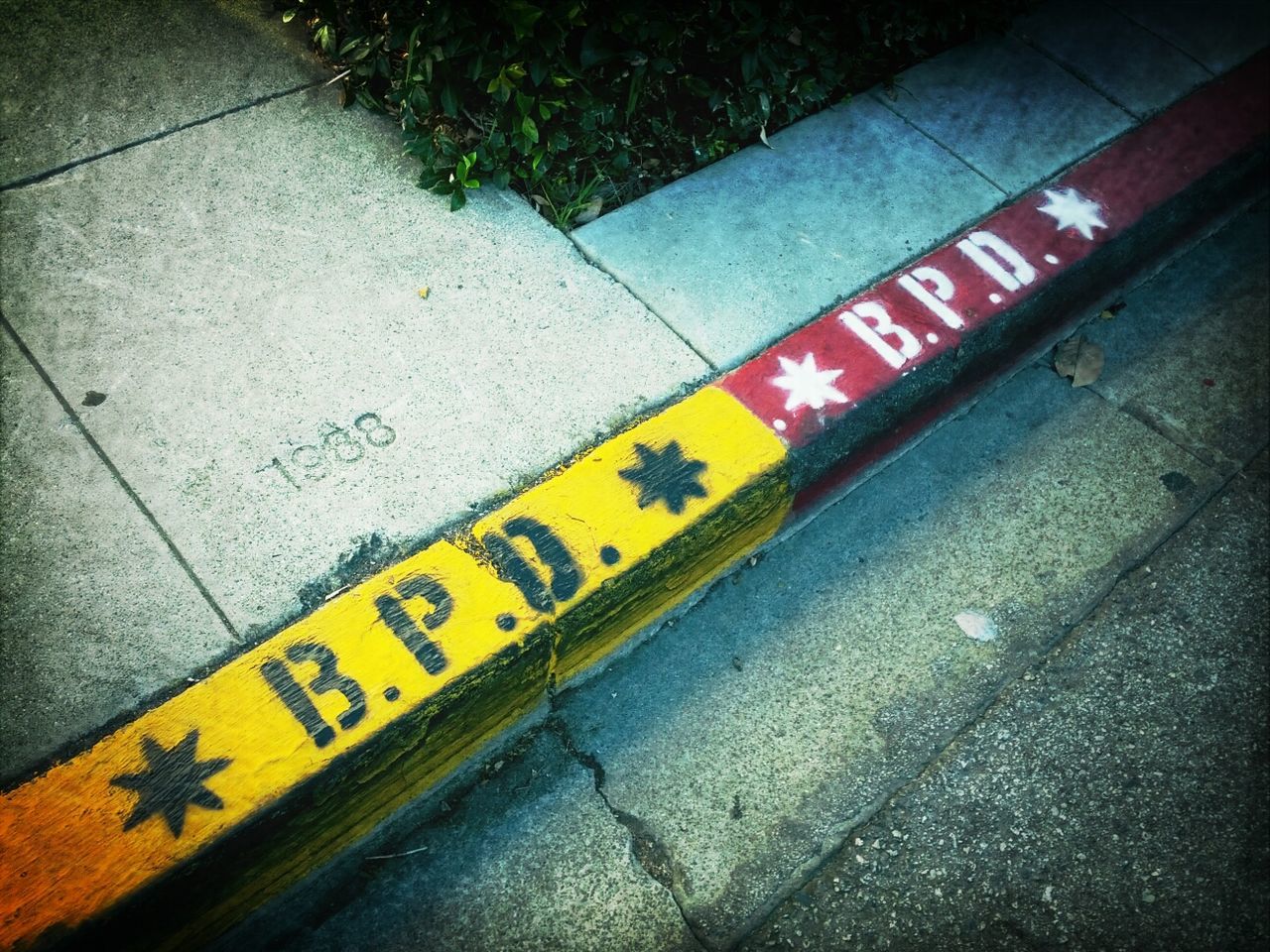 yellow, high angle view, text, street, western script, wall - building feature, transportation, communication, outdoors, day, sidewalk, graffiti, no people, flooring, tiled floor, tile, road, paving stone, built structure, road marking