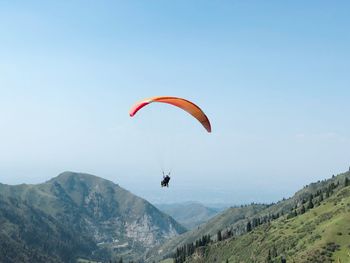 Person paragliding over mountains against sky