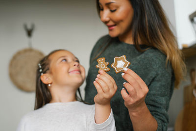 Smiling mom and her daughter are holding christmas cookies in their kitchen