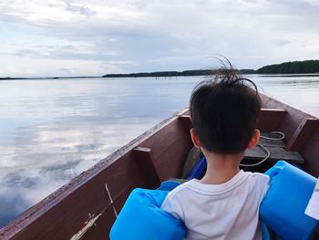 Rear view of boy sailing boat in sea against sky