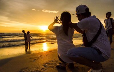 People at beach against sky during sunset