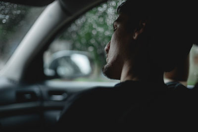 A young guy sits thoughtfully in the car.