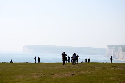 Group of people on land by sea against clear sky