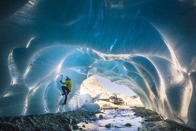 Man ice climbs inside glacial cave during helicopter adventure tour.