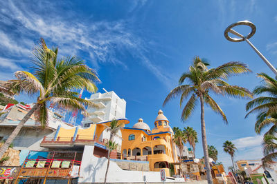 Low angle view of palm trees and buildings against blue sky