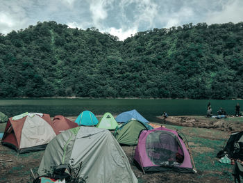 Tents by lake in forest against sky