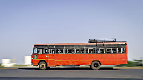 Background blur, pan image of non air-conditioned ,speeding red intercity bus in  maharashtra.