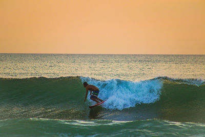 Man surfing in sea against sky during sunset