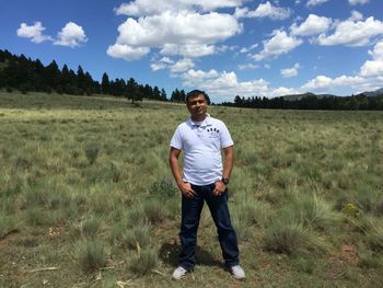 Portrait of confident man standing on field against sky