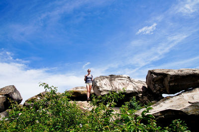 Female hiker standing on rock formation against sky during sunny day