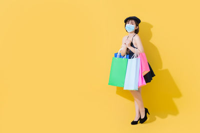 Full length of man holding umbrella standing against yellow background