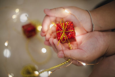 Cropped hands of person holding christmas present with illuminated fairy lights at home