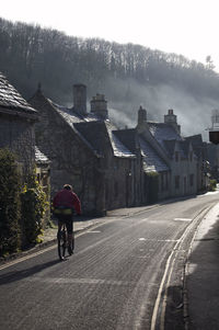 Rear view of man riding bicycle on road amidst buildings