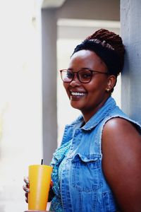 Portrait of smiling young woman with drink standing at home