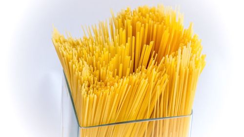 Close-up of raw spaghetti in glass container against white background