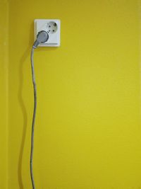 Close-up of electric plug against yellow wall