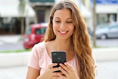 Smiling young woman using mobile phone in city