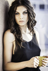 Portrait of young woman holding coffee cup by wall