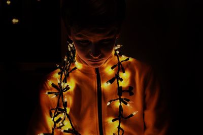 Close-up of boy with illuminated string lights in darkroom