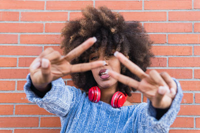 Latin woman with afro hair looking at camera while shows peace gesture with red headphones