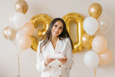 Positive woman celebrating anniversary dressed in stylish feather dress posing with birthday candle