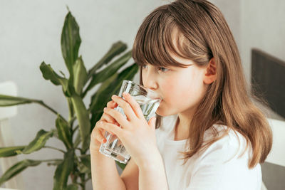 A girl in the kitchen drinks clean water from a glass glass. the importance of water for children