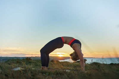 Full length of woman exercising on field against sky during sunset