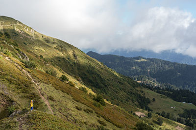 Young woman in yellow hoodie with backpack hiking in picturesque mountain valley healthy lifestyle