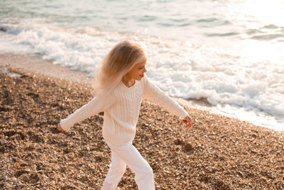 Stylish child girl 5-6 year old wear white knit sweater and pants walking over sea shore background