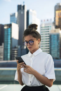 Businesswoman using mobile phone against buildings