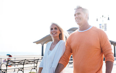 Portrait of smiling woman with man standing on promenade at beach