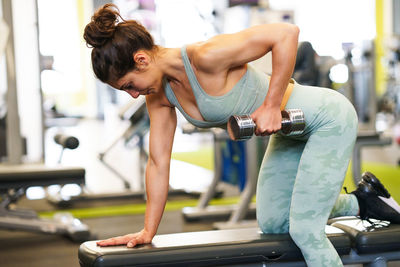 Side view of young woman lifting dumbbell in gym